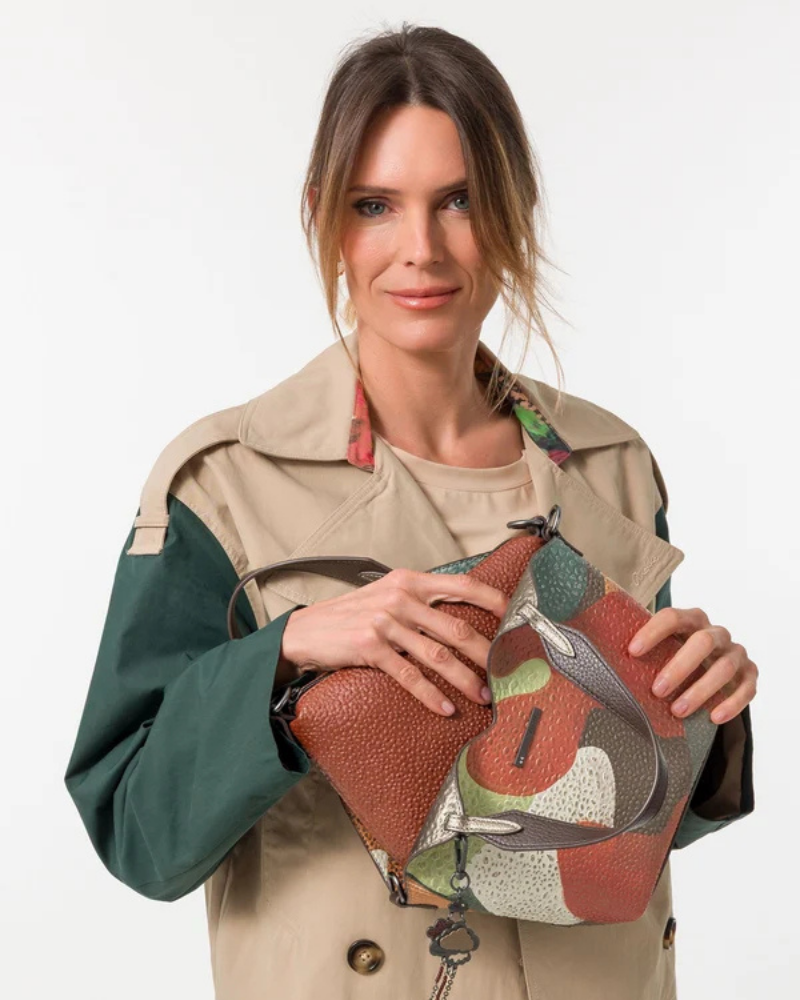 Esta carteira redefine o conceito de versatilidade com uma proposta única: duas carteiras numa só.

A bolsa principal impressiona pelo seu padrão artístico em tons de laranja, verde, bege e terracota, com uma textura trabalhada que evoca o espírito aventureiro e cosmopolita da coleção Odyssey. Os detalhes em metal gunmetal, a corrente com pendente em forma de nuvem e as alças em couro sintético castanho-escuro completam um visual rico e distinto.