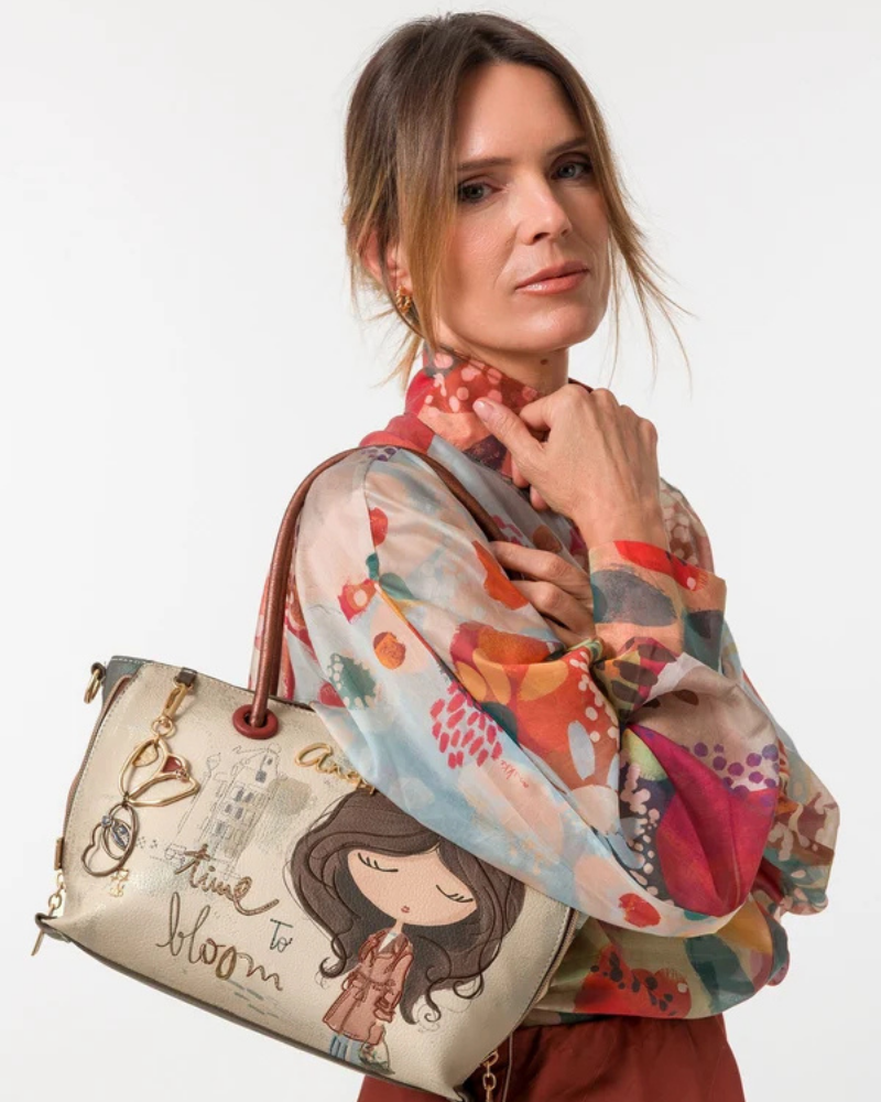 Esta mala de mão transforma a poesia em acessório de moda.

Com o inconfundível painel ilustrado da coleção Tulip — a personagem Anekke numa cena urbana e sonhadora, acompanhada pela frase "time to bloom" —, esta carteira carrega consigo uma mensagem de otimismo e leveza que se sente a cada uso. Os tons creme e castanho, combinados com os detalhes em metal dourado e o pendente em forma de bicicleta, evocam o charme das ruas europeias e a elegância do detalhe artesanal.