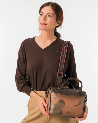 Uma carteira que carrega consigo o espírito da viagem e a sofisticação do detalhe bem executado.

O seu exterior combina couro sintético em tons de bronze envelhecido e castanho-escuro, com aplicações em relevo de motivos florais gravados e silhuetas orgânicas em técnica patchwork — uma composição que evoca mapas antigos, diários de viagem e a beleza do encontro entre culturas. A assinatura Anekke em metal gunmetal e os fechos e argolas em tom escuro completam uma estética coesa e premium.