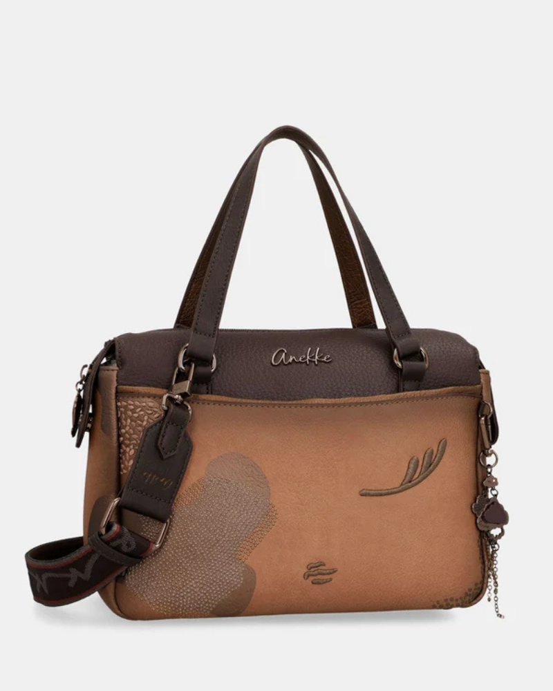 Uma carteira que carrega consigo o espírito da viagem e a sofisticação do detalhe bem executado.

O seu exterior combina couro sintético em tons de bronze envelhecido e castanho-escuro, com aplicações em relevo de motivos florais gravados e silhuetas orgânicas em técnica patchwork — uma composição que evoca mapas antigos, diários de viagem e a beleza do encontro entre culturas. A assinatura Anekke em metal gunmetal e os fechos e argolas em tom escuro completam uma estética coesa e premium.
