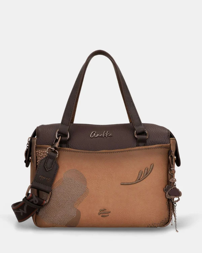 Uma carteira que carrega consigo o espírito da viagem e a sofisticação do detalhe bem executado.

O seu exterior combina couro sintético em tons de bronze envelhecido e castanho-escuro, com aplicações em relevo de motivos florais gravados e silhuetas orgânicas em técnica patchwork — uma composição que evoca mapas antigos, diários de viagem e a beleza do encontro entre culturas. A assinatura Anekke em metal gunmetal e os fechos e argolas em tom escuro completam uma estética coesa e premium.