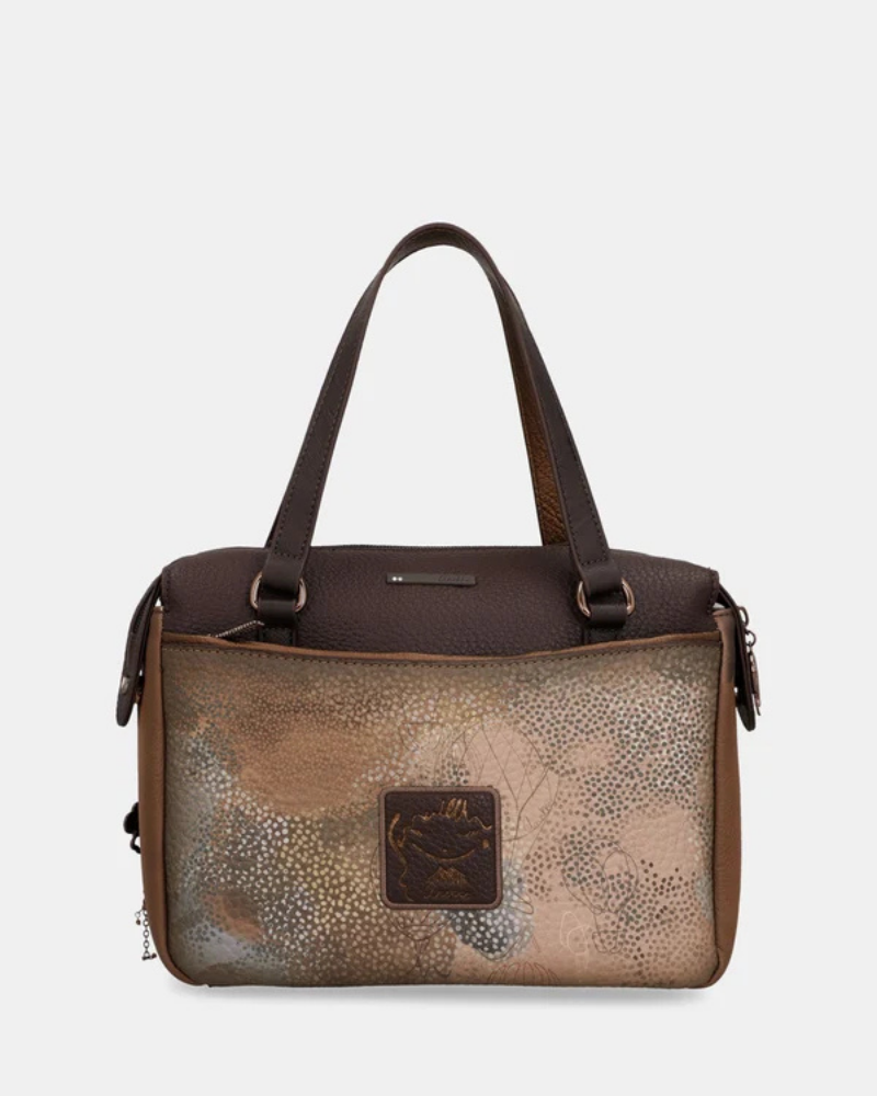 Uma carteira que carrega consigo o espírito da viagem e a sofisticação do detalhe bem executado.

O seu exterior combina couro sintético em tons de bronze envelhecido e castanho-escuro, com aplicações em relevo de motivos florais gravados e silhuetas orgânicas em técnica patchwork — uma composição que evoca mapas antigos, diários de viagem e a beleza do encontro entre culturas. A assinatura Anekke em metal gunmetal e os fechos e argolas em tom escuro completam uma estética coesa e premium.