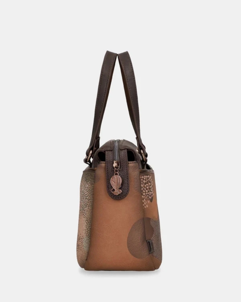 Uma carteira que carrega consigo o espírito da viagem e a sofisticação do detalhe bem executado.

O seu exterior combina couro sintético em tons de bronze envelhecido e castanho-escuro, com aplicações em relevo de motivos florais gravados e silhuetas orgânicas em técnica patchwork — uma composição que evoca mapas antigos, diários de viagem e a beleza do encontro entre culturas. A assinatura Anekke em metal gunmetal e os fechos e argolas em tom escuro completam uma estética coesa e premium.