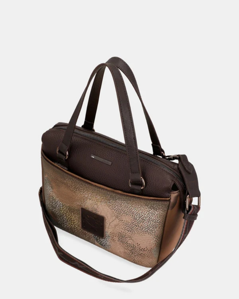 Uma carteira que carrega consigo o espírito da viagem e a sofisticação do detalhe bem executado.

O seu exterior combina couro sintético em tons de bronze envelhecido e castanho-escuro, com aplicações em relevo de motivos florais gravados e silhuetas orgânicas em técnica patchwork — uma composição que evoca mapas antigos, diários de viagem e a beleza do encontro entre culturas. A assinatura Anekke em metal gunmetal e os fechos e argolas em tom escuro completam uma estética coesa e premium.