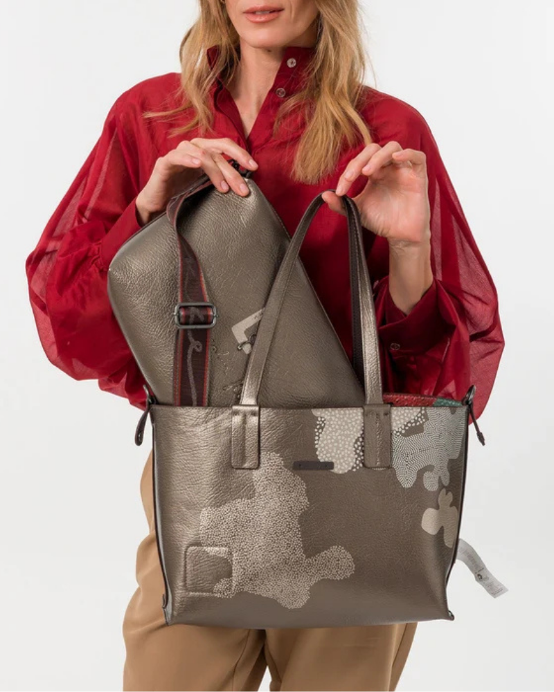 Esta carteira é muito mais do que uma carteira: é um conjunto reversível e modular que oferece duas personalidades num só produto.

A tote principal destaca-se pelo seu padrão artístico em tons de terracota, verde-musgo, laranja e creme, com formas abstratas e texturas em relevo que evocam uma pintura contemporânea. As asas duplas em castanho-escuro, os fechos e argolas em metal gunmetal e o pendente de chaves decorativo completam o design com um toque boémio e editorial.