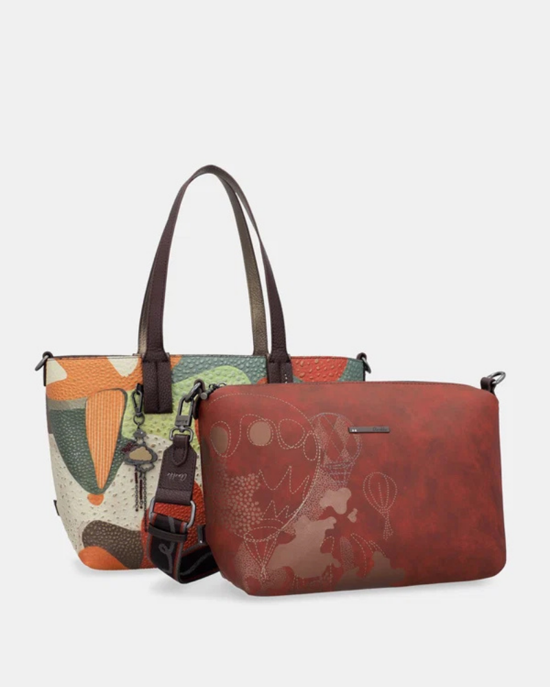 Esta carteira é muito mais do que uma carteira: é um conjunto reversível e modular que oferece duas personalidades num só produto.

A tote principal destaca-se pelo seu padrão artístico em tons de terracota, verde-musgo, laranja e creme, com formas abstratas e texturas em relevo que evocam uma pintura contemporânea. As asas duplas em castanho-escuro, os fechos e argolas em metal gunmetal e o pendente de chaves decorativo completam o design com um toque boémio e editorial.