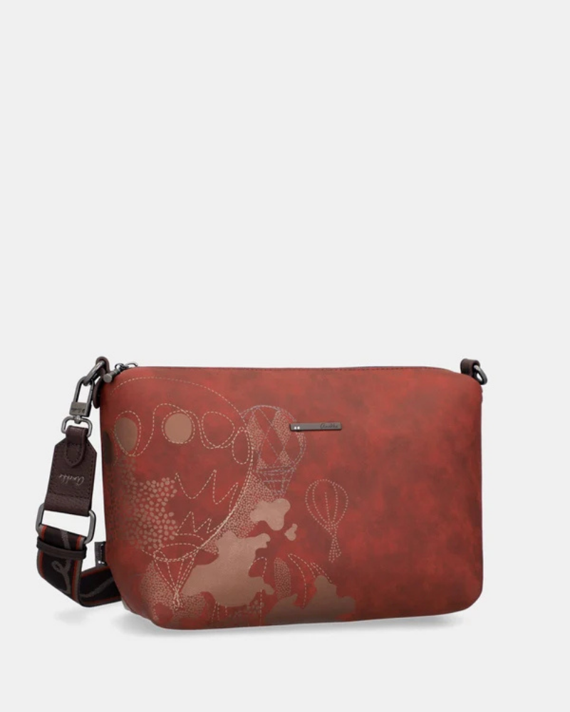 Esta carteira é muito mais do que uma carteira: é um conjunto reversível e modular que oferece duas personalidades num só produto.

A tote principal destaca-se pelo seu padrão artístico em tons de terracota, verde-musgo, laranja e creme, com formas abstratas e texturas em relevo que evocam uma pintura contemporânea. As asas duplas em castanho-escuro, os fechos e argolas em metal gunmetal e o pendente de chaves decorativo completam o design com um toque boémio e editorial.