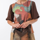 Uma carteira de carácter aventureiro e acabamento sofisticado.

Construída em patchwork de materiais sintéticos com diferentes texturas — grão fino, superfície metálica em cobre envelhecido e painel com estampado pontilhado iridescente —, esta mala de mão combina profundidade visual com uma silhueta estruturada e geométrica.