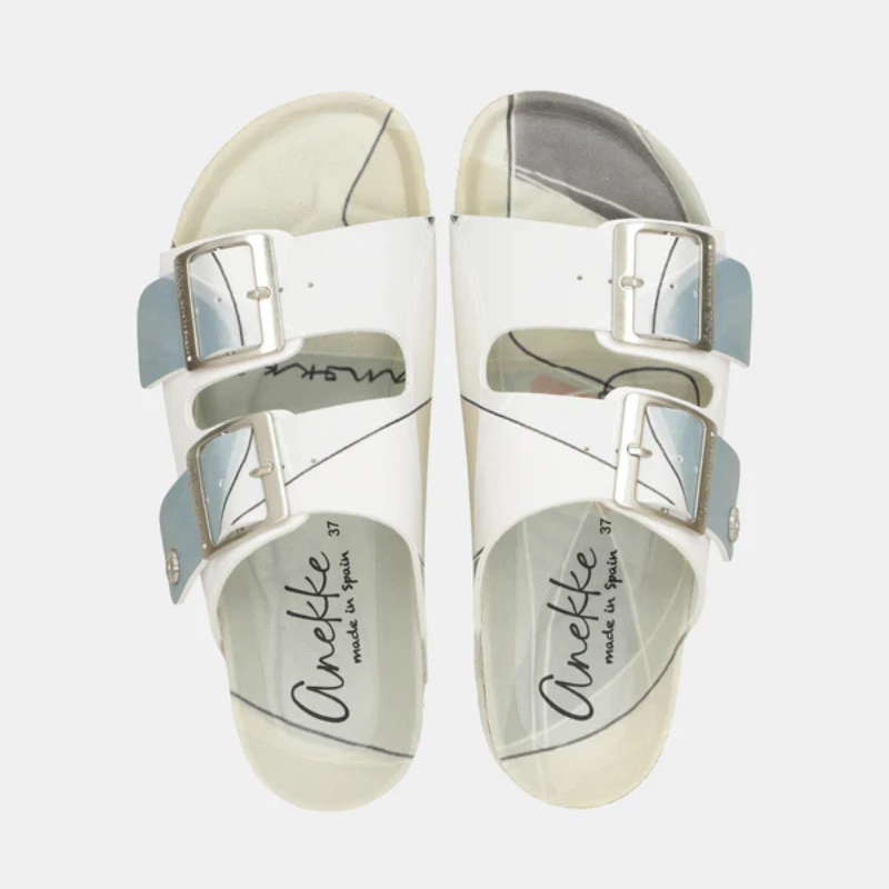 Um chinelo que une elegância e leveza numa só peça.

As tiras em branco com reflexo iridescente azul-prata captam a luz de forma única, enquanto as fivelas metálicas prateadas de grande formato acrescentam um toque contemporâneo e sofisticado. A palmilha anatómica adapta-se ao formato do pé, garantindo um conforto excepcional do primeiro ao último passo, e a sola branca em borracha assegura estabilidade em qualquer superfície.
