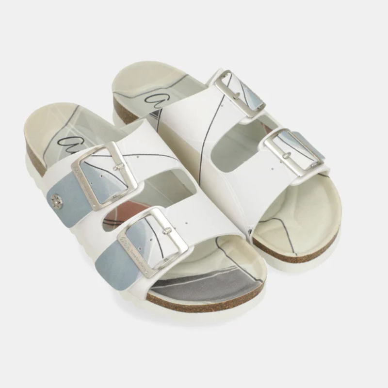Um chinelo que une elegância e leveza numa só peça.

As tiras em branco com reflexo iridescente azul-prata captam a luz de forma única, enquanto as fivelas metálicas prateadas de grande formato acrescentam um toque contemporâneo e sofisticado. A palmilha anatómica adapta-se ao formato do pé, garantindo um conforto excepcional do primeiro ao último passo, e a sola branca em borracha assegura estabilidade em qualquer superfície.