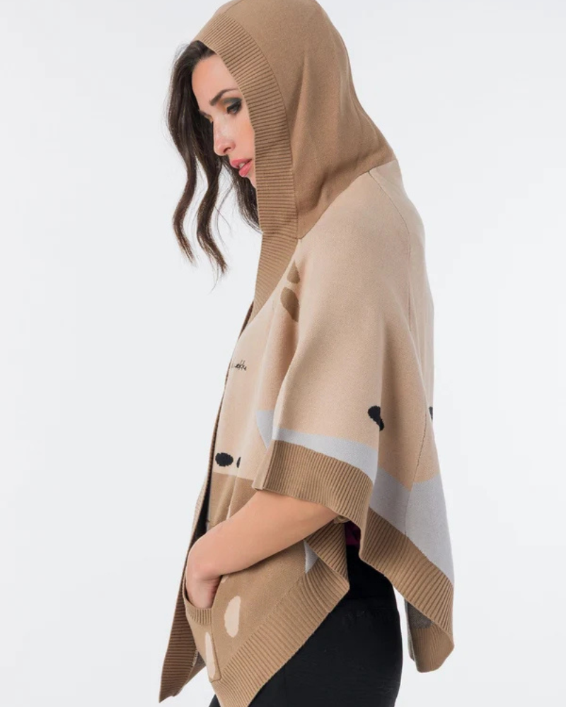 Este poncho é uma peça versátil que combina conforto e sofisticação numa silhueta única.

Confeccionado em malha de qualidade premium, apresenta um padrão exclusivo inspirado na girafa, com manchas em tons de bege, creme e preto que lhe conferem um carácter editorial e atemporal. O capuz estruturado com acabamento em canelado, as mangas curtas amplas e os bolsos frontais tornam-no tão funcional quanto elegante. 