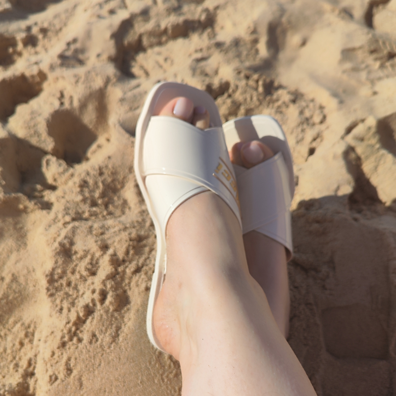 Este chinelo apresenta um design moderno e elegante, ideal para momentos de lazer, especialmente em ambientes de praia ou piscina. O chinelo possui tiras largas cruzadas na parte superior, criando um visual sofisticado e ao mesmo tempo descontraído. A combinação do branco com detalhes dourados faz com que o chinelo seja versátil e fácil de combinar com diversos tipos de roupas de verão.