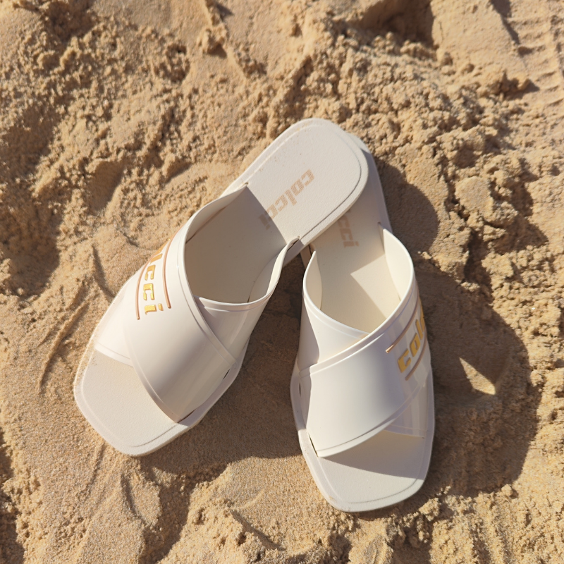 Este chinelo apresenta um design moderno e elegante, ideal para momentos de lazer, especialmente em ambientes de praia ou piscina. O chinelo possui tiras largas cruzadas na parte superior, criando um visual sofisticado e ao mesmo tempo descontraído. A combinação do branco com detalhes dourados faz com que o chinelo seja versátil e fácil de combinar com diversos tipos de roupas de verão.