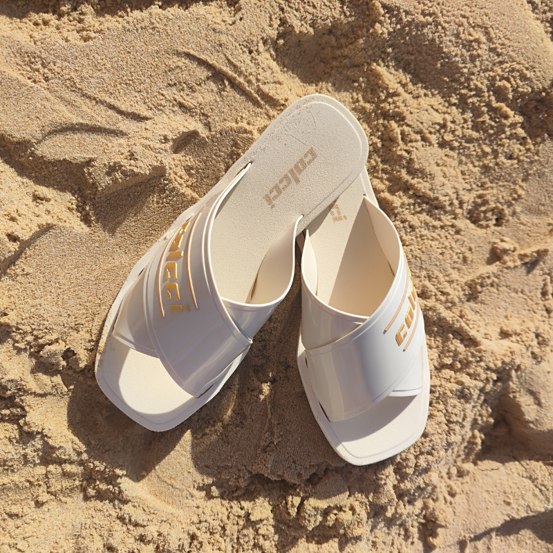 Este chinelo apresenta um design moderno e elegante, ideal para momentos de lazer, especialmente em ambientes de praia ou piscina. O chinelo possui tiras largas cruzadas na parte superior, criando um visual sofisticado e ao mesmo tempo descontraído. A combinação do branco com detalhes dourados faz com que o chinelo seja versátil e fácil de combinar com diversos tipos de roupas de verão.