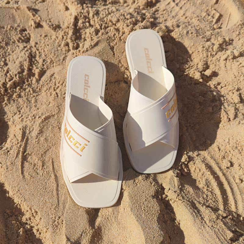 Este chinelo apresenta um design moderno e elegante, ideal para momentos de lazer, especialmente em ambientes de praia ou piscina. O chinelo possui tiras largas cruzadas na parte superior, criando um visual sofisticado e ao mesmo tempo descontraído. A combinação do branco com detalhes dourados faz com que o chinelo seja versátil e fácil de combinar com diversos tipos de roupas de verão.