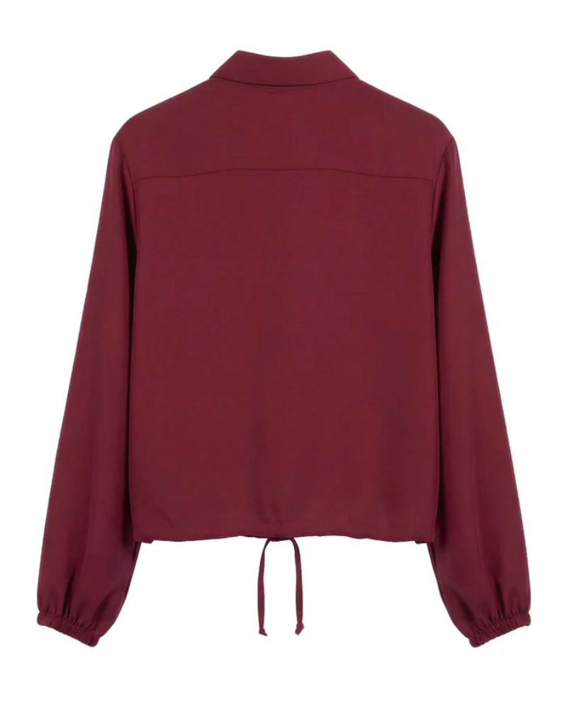 Este camiseiro combina um design clássico com um toque moderno e feminino.

Apresenta gola tradicional, fecho frontal com botões e mangas compridas com punhos ligeiramente franzidos, enquanto o cordão de ajuste na parte inferior permite definir a silhueta e adaptar o caimento ao gosto de cada pessoa.