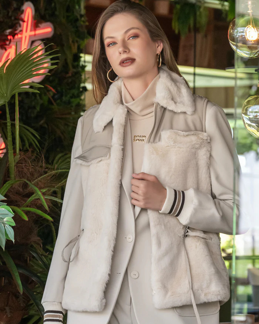 Este colete em tom bege com aplicação de pelo macio na parte frontal e no colarinho, oferece um equilíbrio perfeito entre elegância e conforto.

O design inclui detalhes funcionais, como bolsos laterais e fecho lateral ajustável, que acrescentam versatilidade à peça.