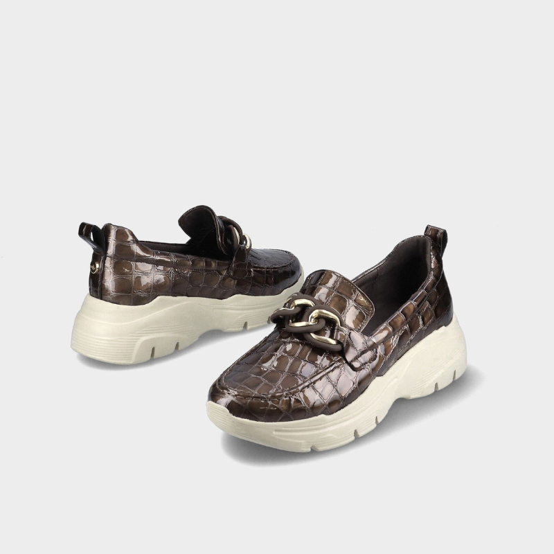 Este mocassim destaca-se pelo acabamento castanho-escuro brilhante com efeito croco, que confere um toque sofisticado e distinto ao modelo.

O detalhe da corrente dourada sobre a pala acrescenta elegância, enquanto a sola robusta em tom cru, com piso tratorado, cria um contraste moderno e atual.