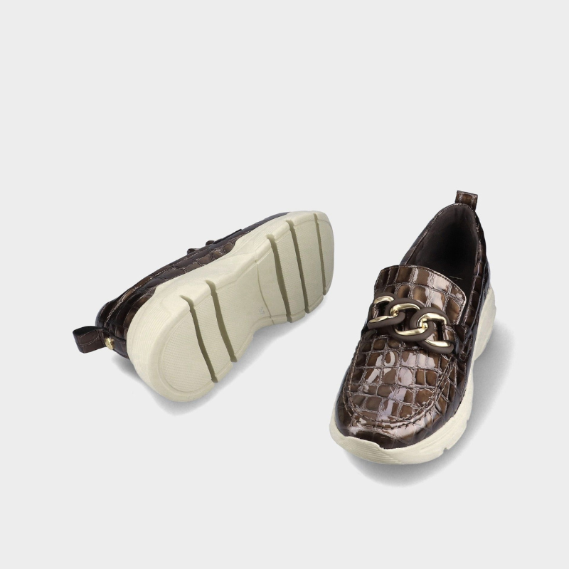 Este mocassim destaca-se pelo acabamento castanho-escuro brilhante com efeito croco, que confere um toque sofisticado e distinto ao modelo.

O detalhe da corrente dourada sobre a pala acrescenta elegância, enquanto a sola robusta em tom cru, com piso tratorado, cria um contraste moderno e atual.