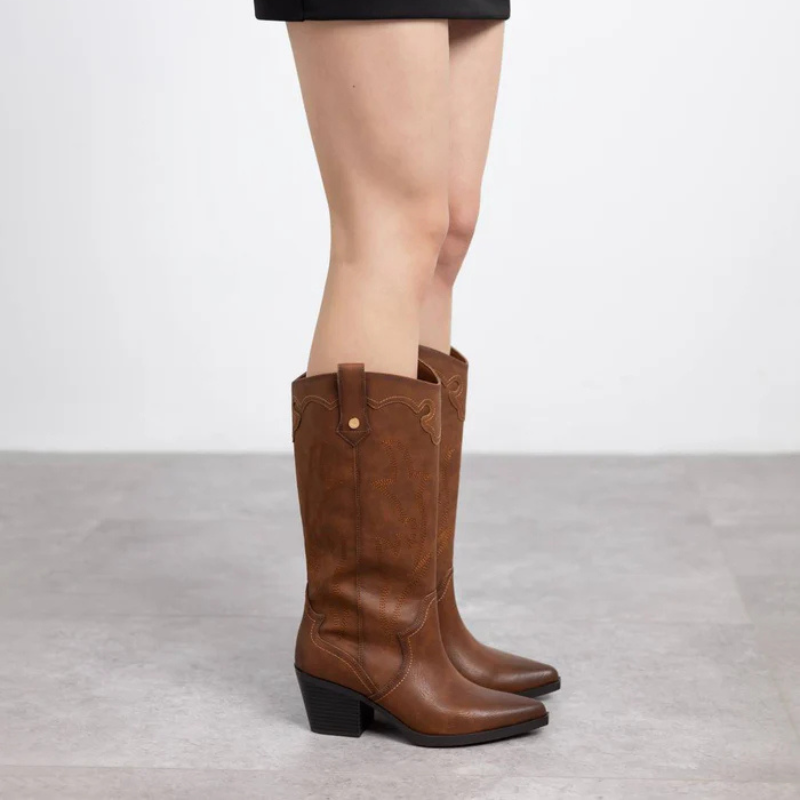 Esta bota texana de cano alto é a escolha perfeita para quem deseja um estilo marcante e versátil.

Produzida em material sintético de alta qualidade, ela apresenta acabamento em tom terroso e detalhes de bordados que valorizam seu design clássico western. O salto bloco médio garante conforto e estabilidade, permitindo o uso prolongado sem esquecer a elegância. Com forma bicuda levemente afinada e puxadores laterais, facilita o calçar e adiciona personalidade ao visual.