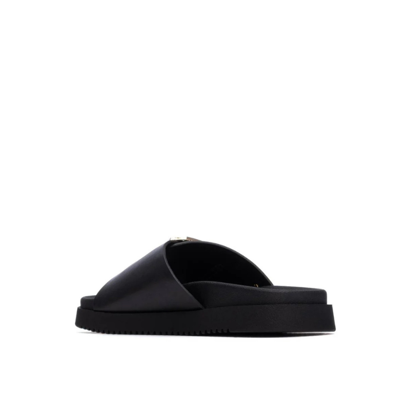 Minimalista e com um impacto visual inegável, este chinelo plano em preto é uma peça que redefine o conceito de casual chic.

A tira larga e estruturada, decorada com uma fivela oversized em dourado, transforma um modelo de inspiração clássica numa declaração de estilo contemporânea. A sola plataforma em borracha preta, ligeiramente elevada, confere conforto e estabilidade ao longo do dia, enquanto a palmilha macia acompanha o pé com suavidade.