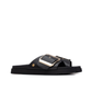 Minimalista e com um impacto visual inegável, este chinelo plano em preto é uma peça que redefine o conceito de casual chic.

A tira larga e estruturada, decorada com uma fivela oversized em dourado, transforma um modelo de inspiração clássica numa declaração de estilo contemporânea. A sola plataforma em borracha preta, ligeiramente elevada, confere conforto e estabilidade ao longo do dia, enquanto a palmilha macia acompanha o pé com suavidade.